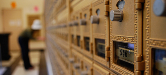 A picture of the JRL mailroom lobby featuring mailboxes on the right, and a person leaning down to open their box on the left.