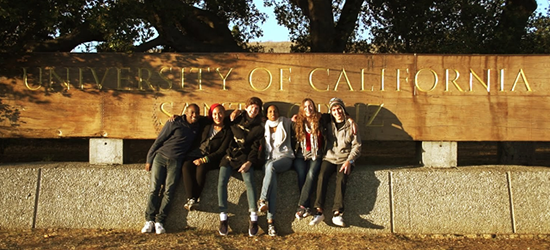 students sitting outside of a welcome to UCSC sign.